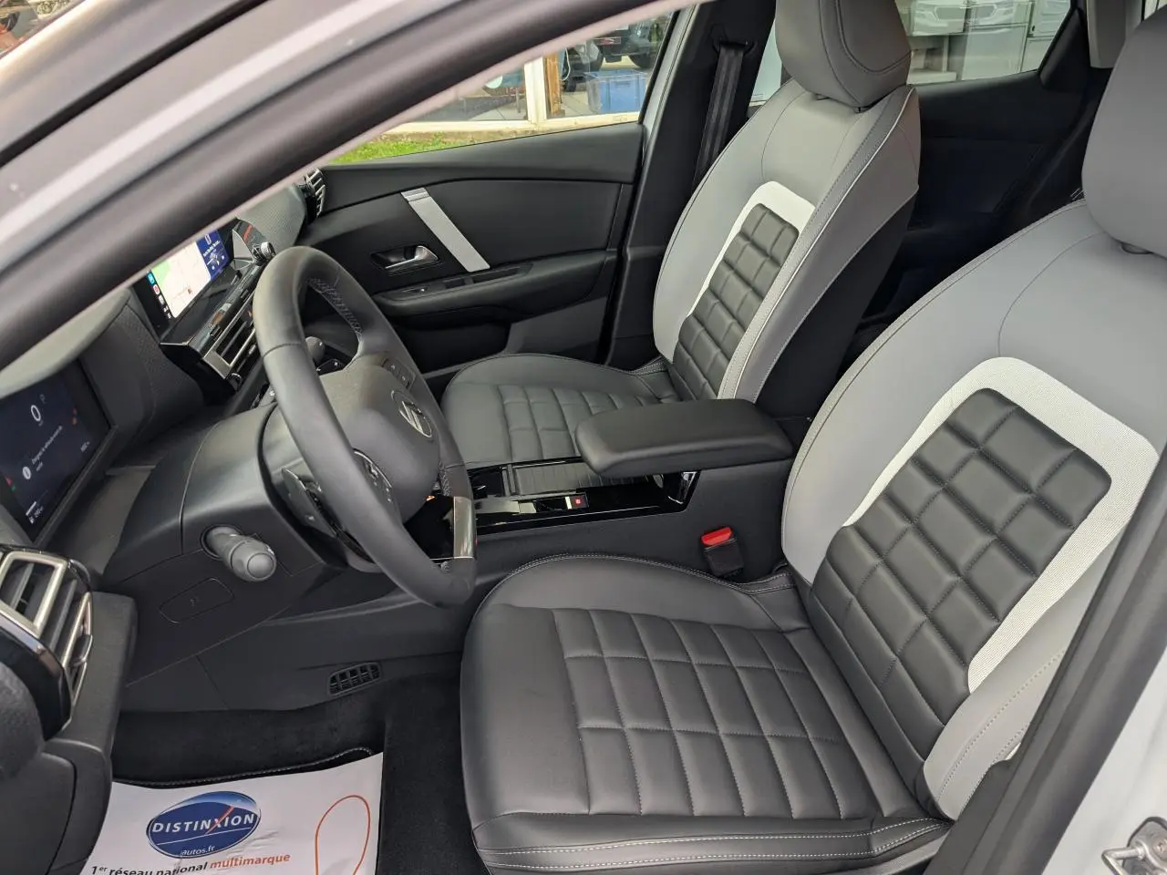 Intérieur de la Citroën C4 2025 vu côté conducteur, sièges gris et noirs avec console centrale noire brillante.
