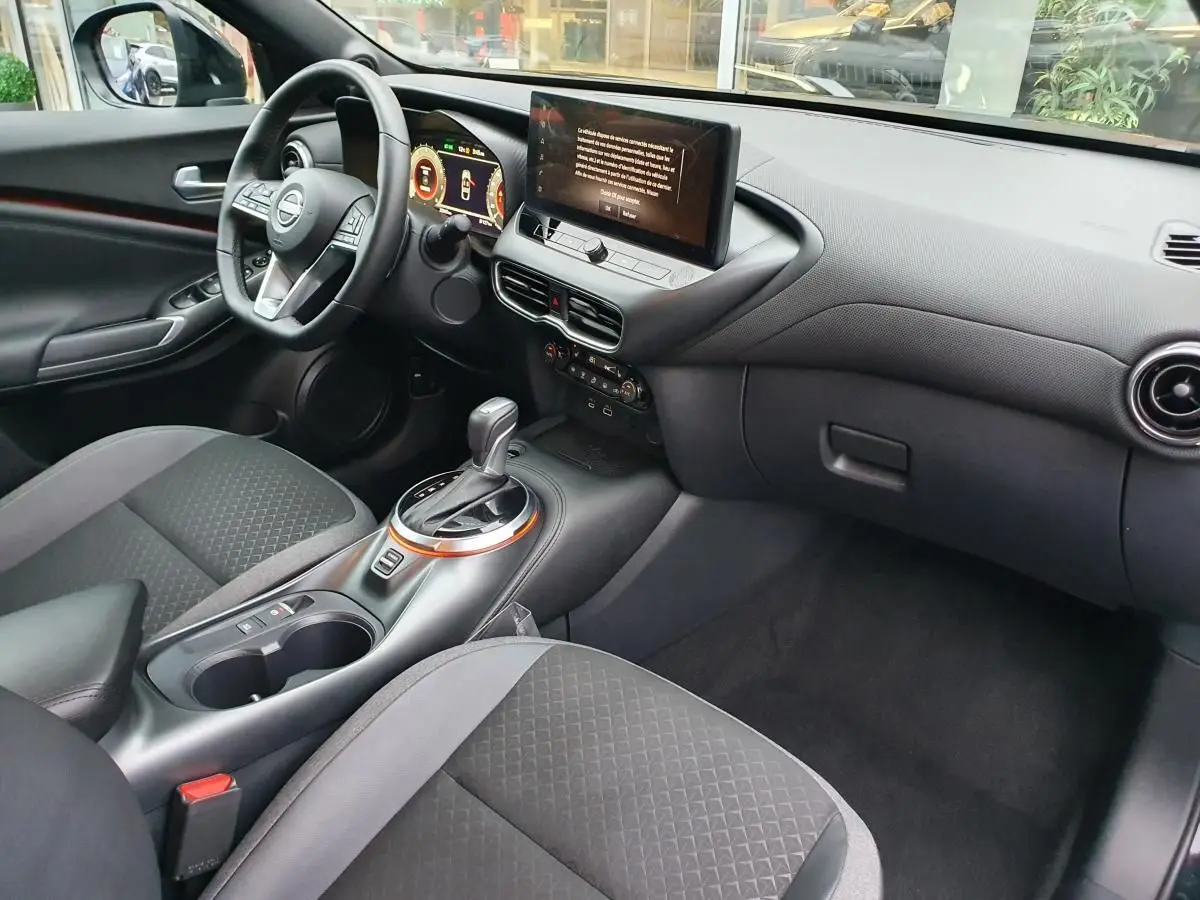 Intérieur avant droit du Nissan Juke 2025 noir, avec console centrale, écran tactile et volant multifonctions.