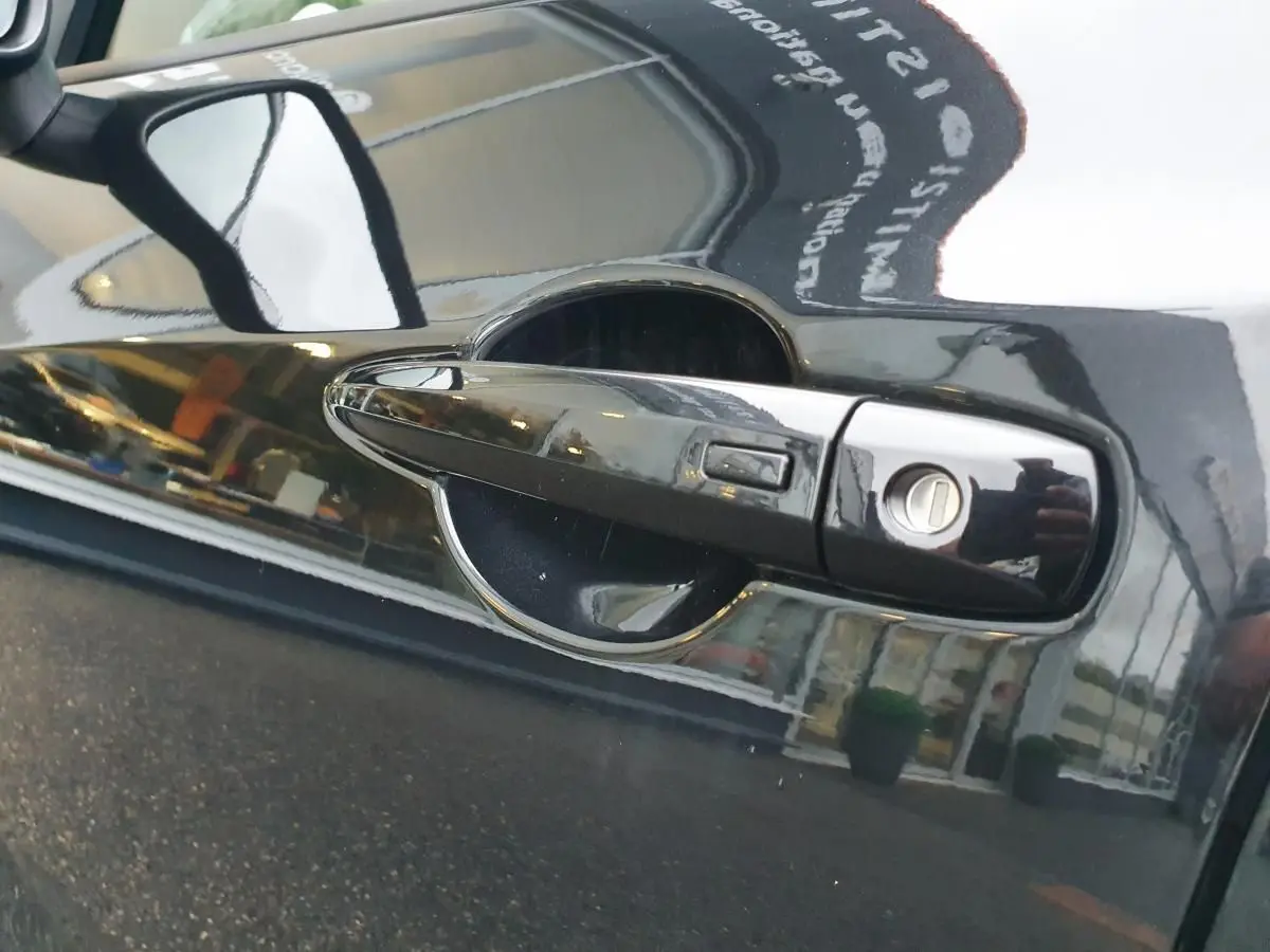 Poignée de porte noire côté gauche du Nissan Juke 2025 avec serrure et rétroviseur latéral réfléchissant.