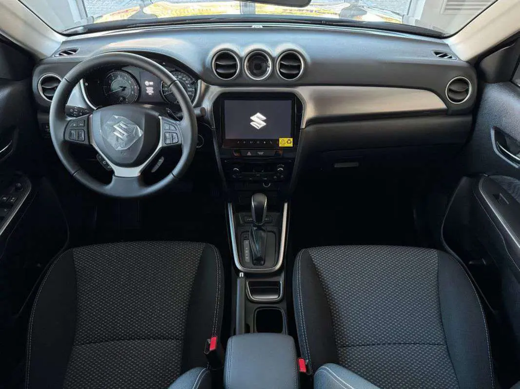 Vue intérieure frontale du Suzuki Vitara 1.4 BVA Privilege AllGrip 2025, tableau de bord noir avec écran tactile central.