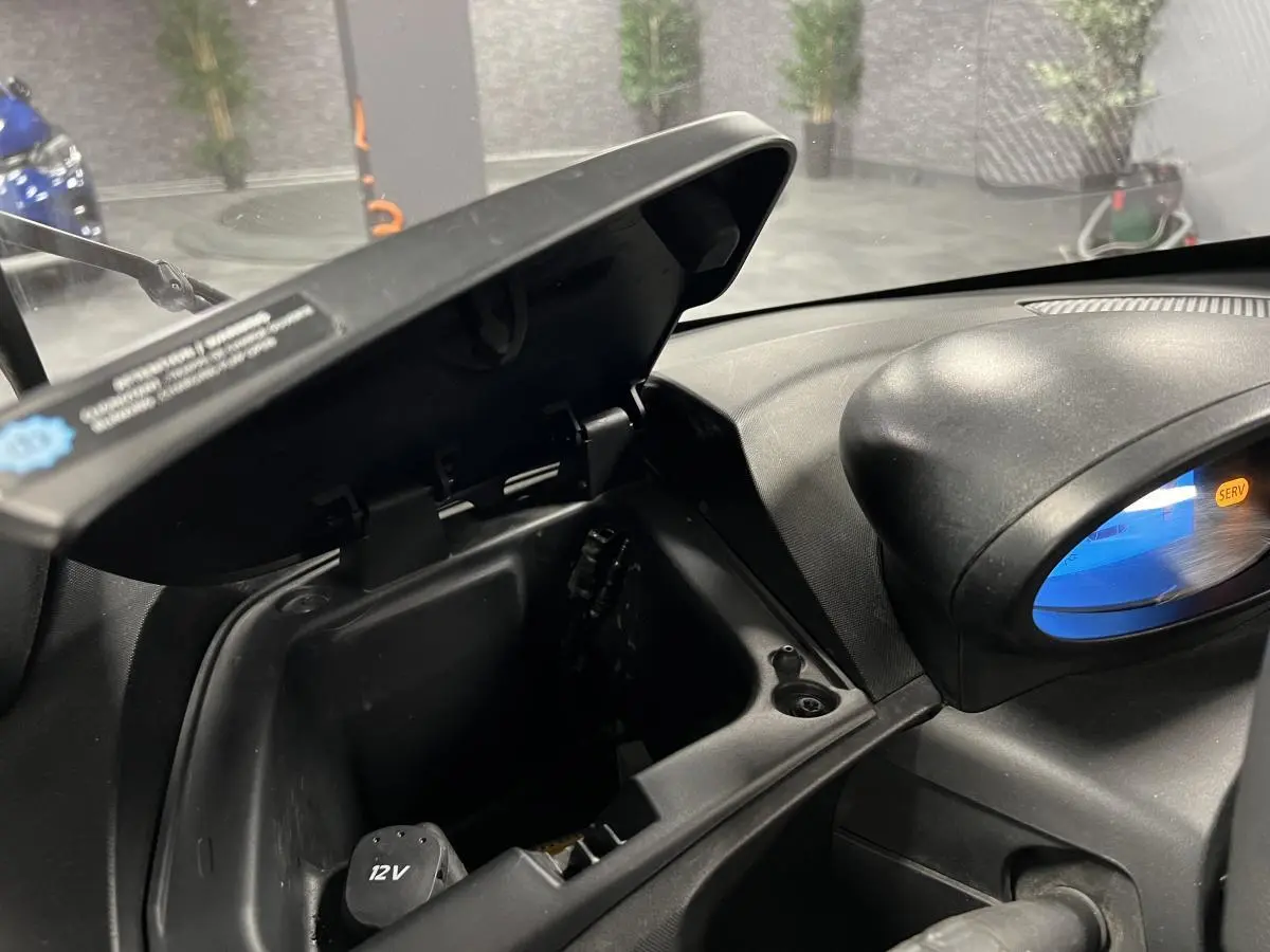 Boîte à gants ouverte côté droit du tableau de bord noir d'une Renault Twizy orange 2019 électrique.