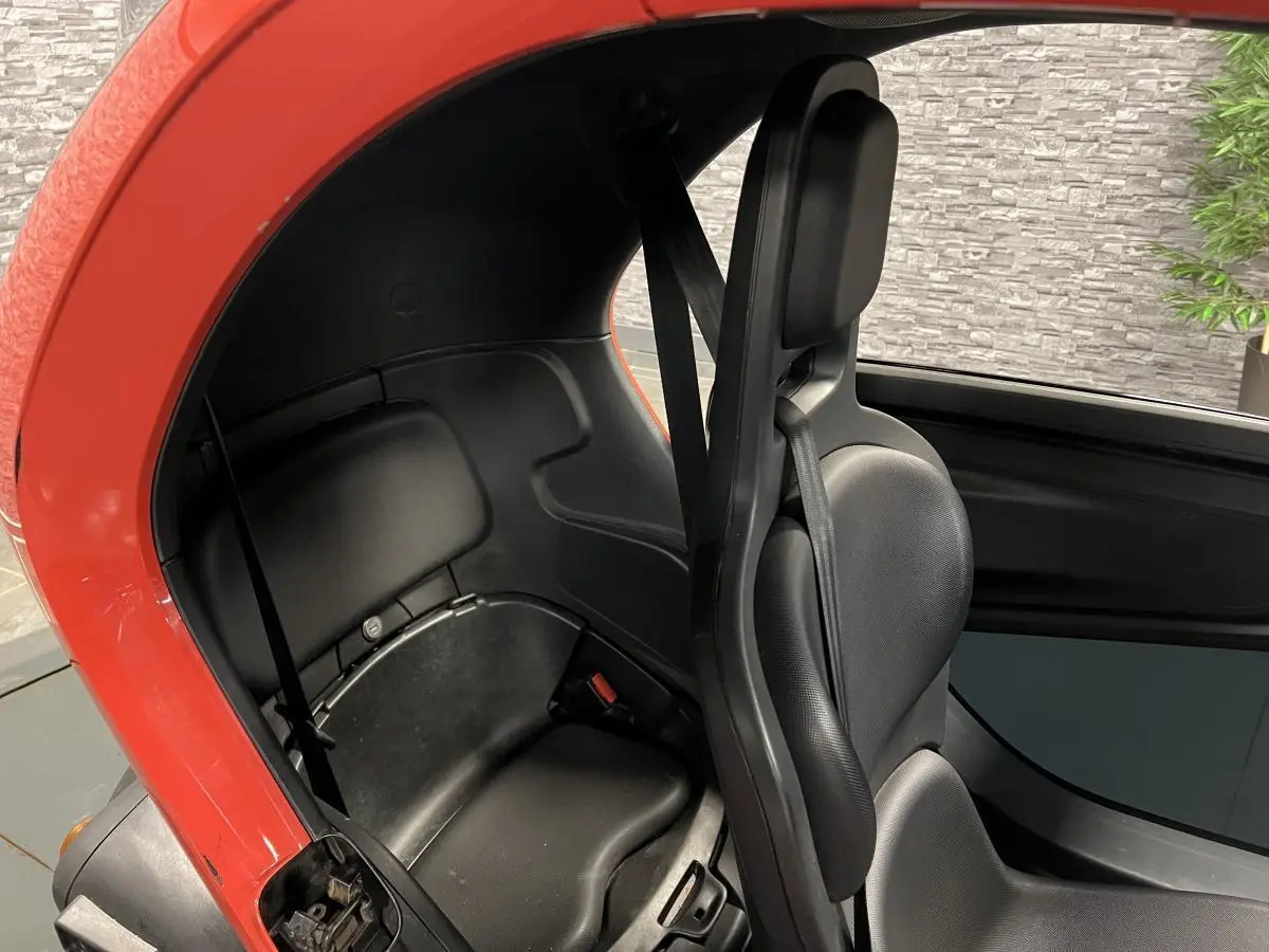 Vue intérieure côté droit du Renault Twizy orange 2019, montrant les sièges noirs compacts et la ceinture de sécurité.