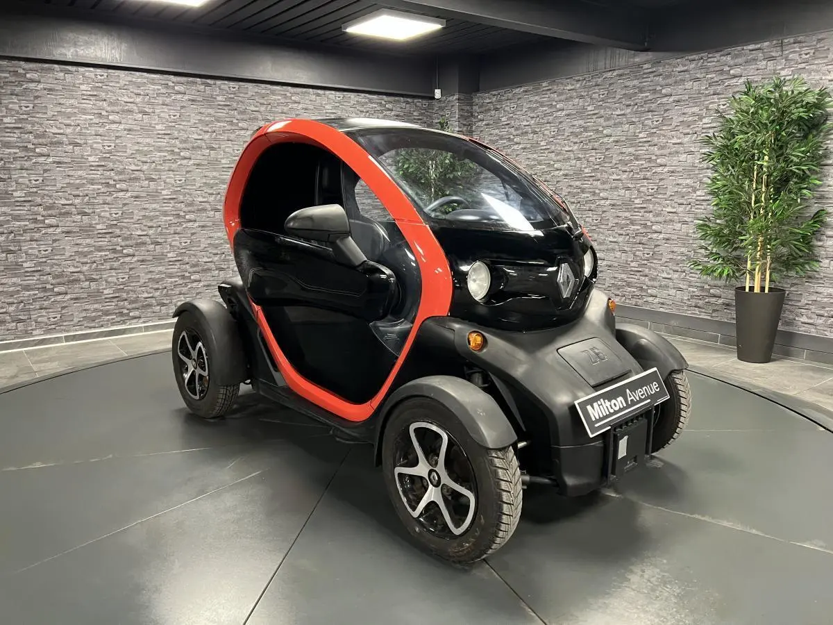 Vue 3/4 avant droite de la Renault Twizy Intens 2019 orange et noire, petite voiture électrique compacte en intérieur showroom.