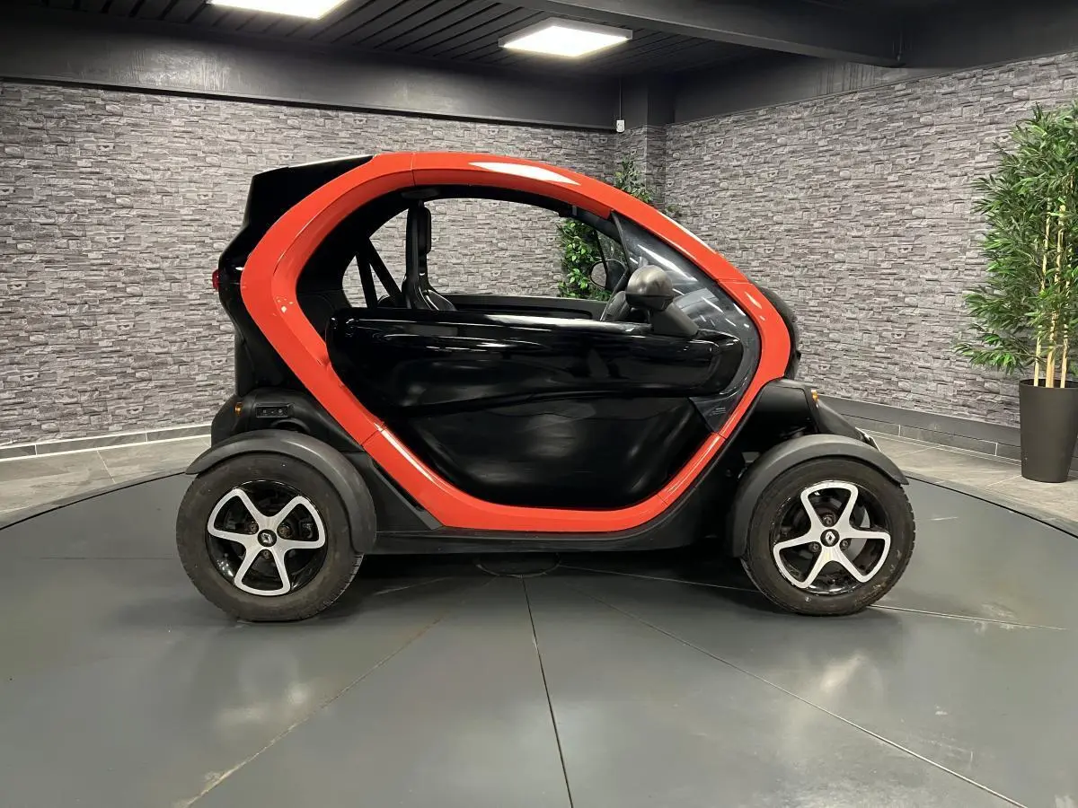 Profil droit de la Renault Twizy Intens 2019 orange et noir, petite voiture électrique compacte en intérieur showroom.