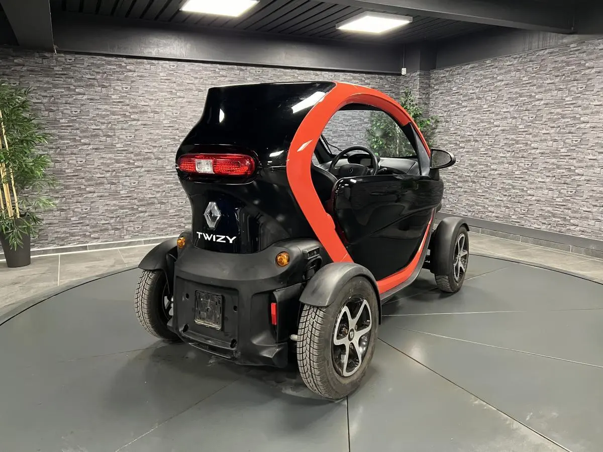 Vue 3/4 arrière droite d'une Renault Twizy orange et noire avec portes élytre dans un showroom intérieur.