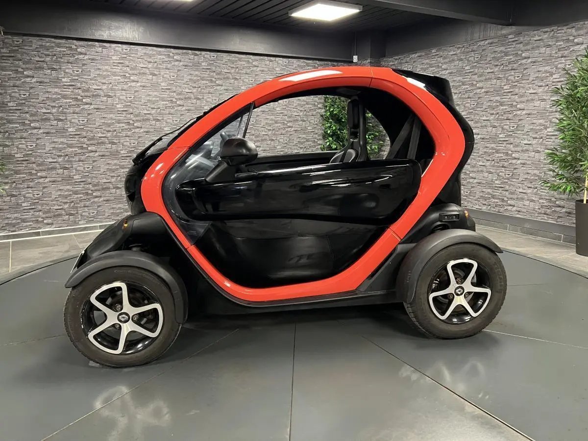 Profil côté gauche de la Renault Twizy Intens 2019 orange et noire, avec portes élytre dans un showroom.