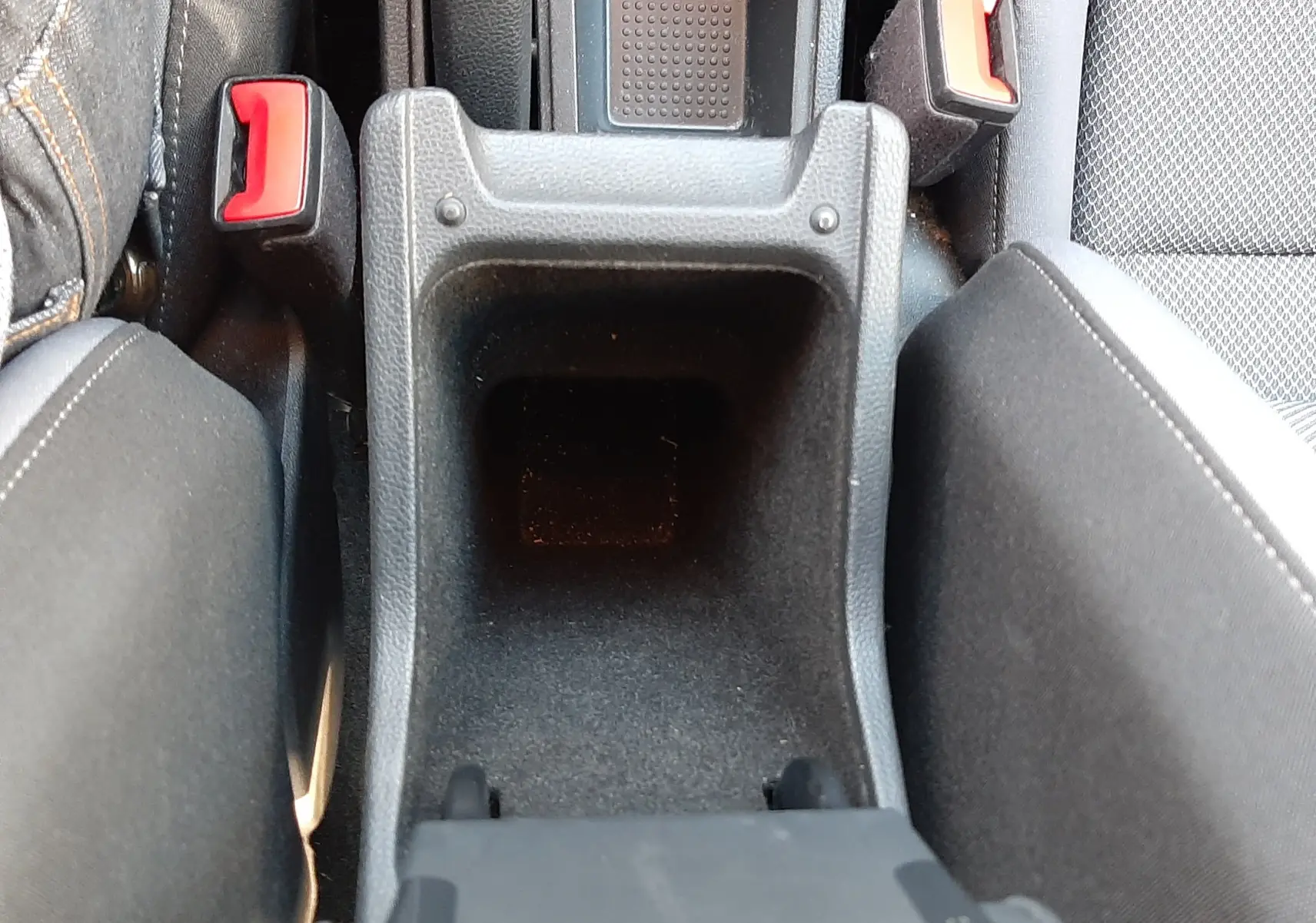 Vue plongeante sur le rangement central noir entre les sièges avant gris tissu du SEAT Arona 2019.