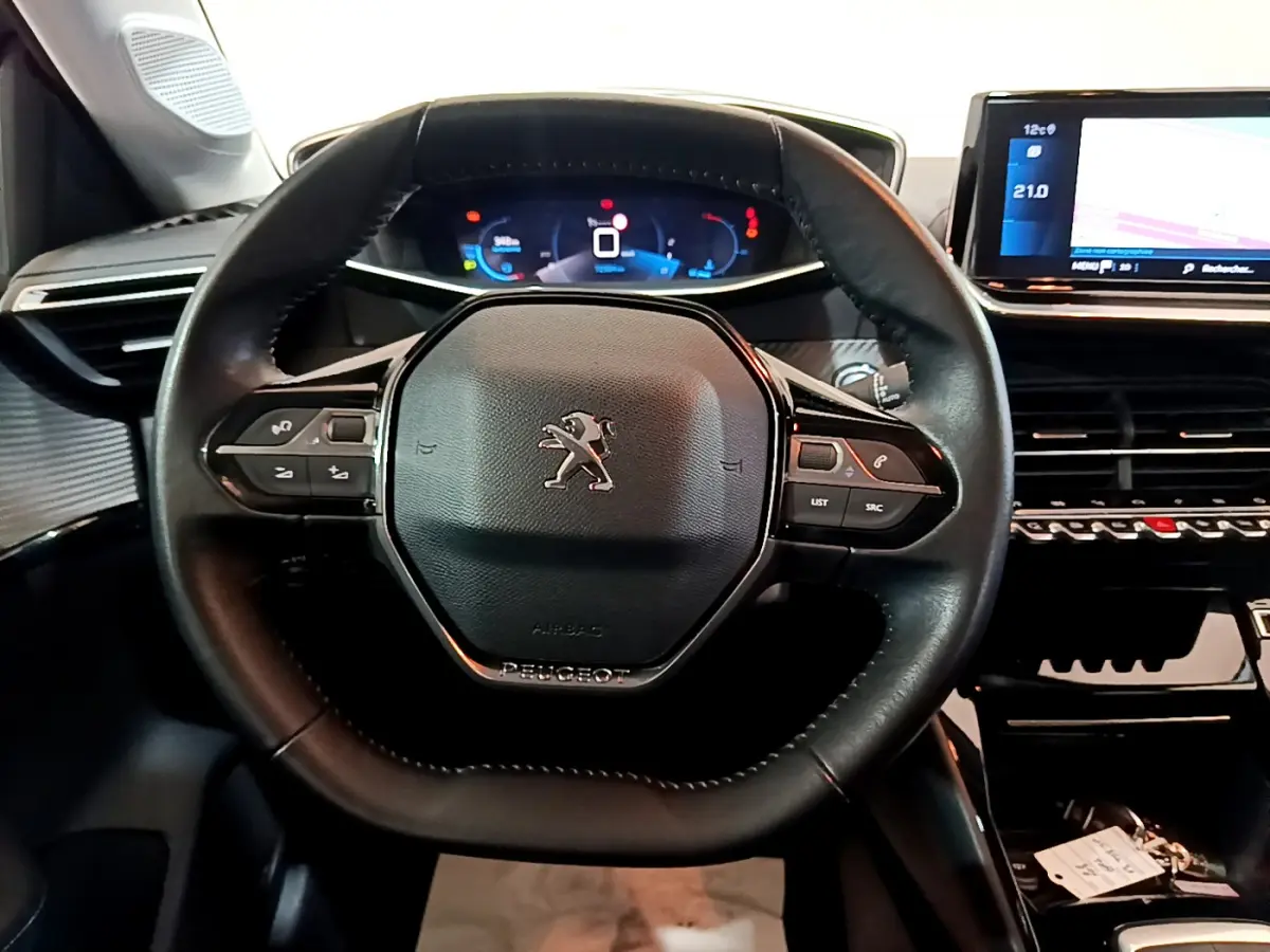 Vue rapprochée du volant cuir noir de la Peugeot 208 PureTech 100, avec tableau de bord numérique et écran tactile visible.