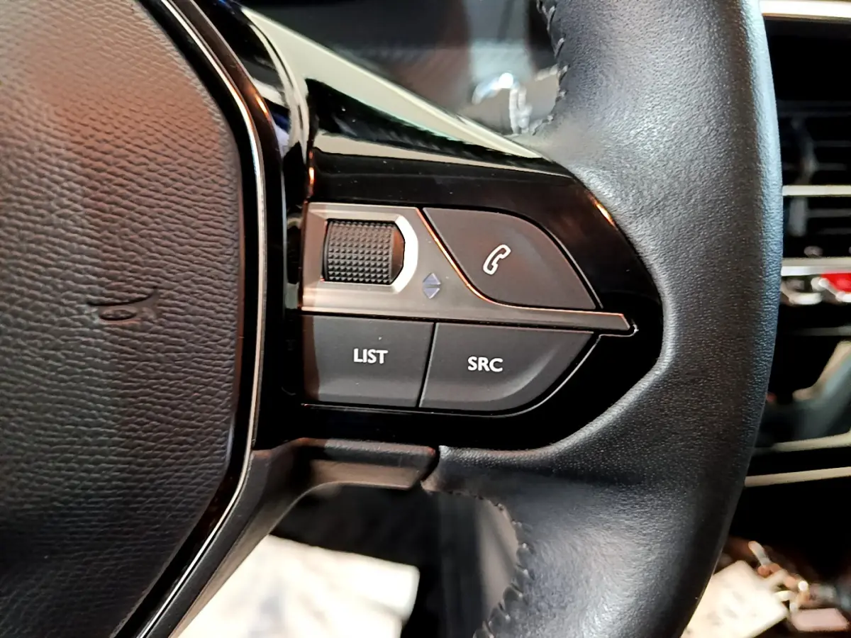 Gros plan sur les commandes gauche du volant cuir noir de la Peugeot 208 gris clair, avec boutons LIST et SRC visibles.
