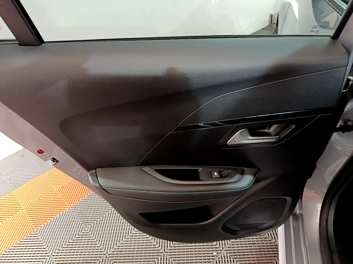 Gros plan sur la porte arrière droite d'une Peugeot 208 gris clair, avec poignée intérieure et bouton de vitre électrique.