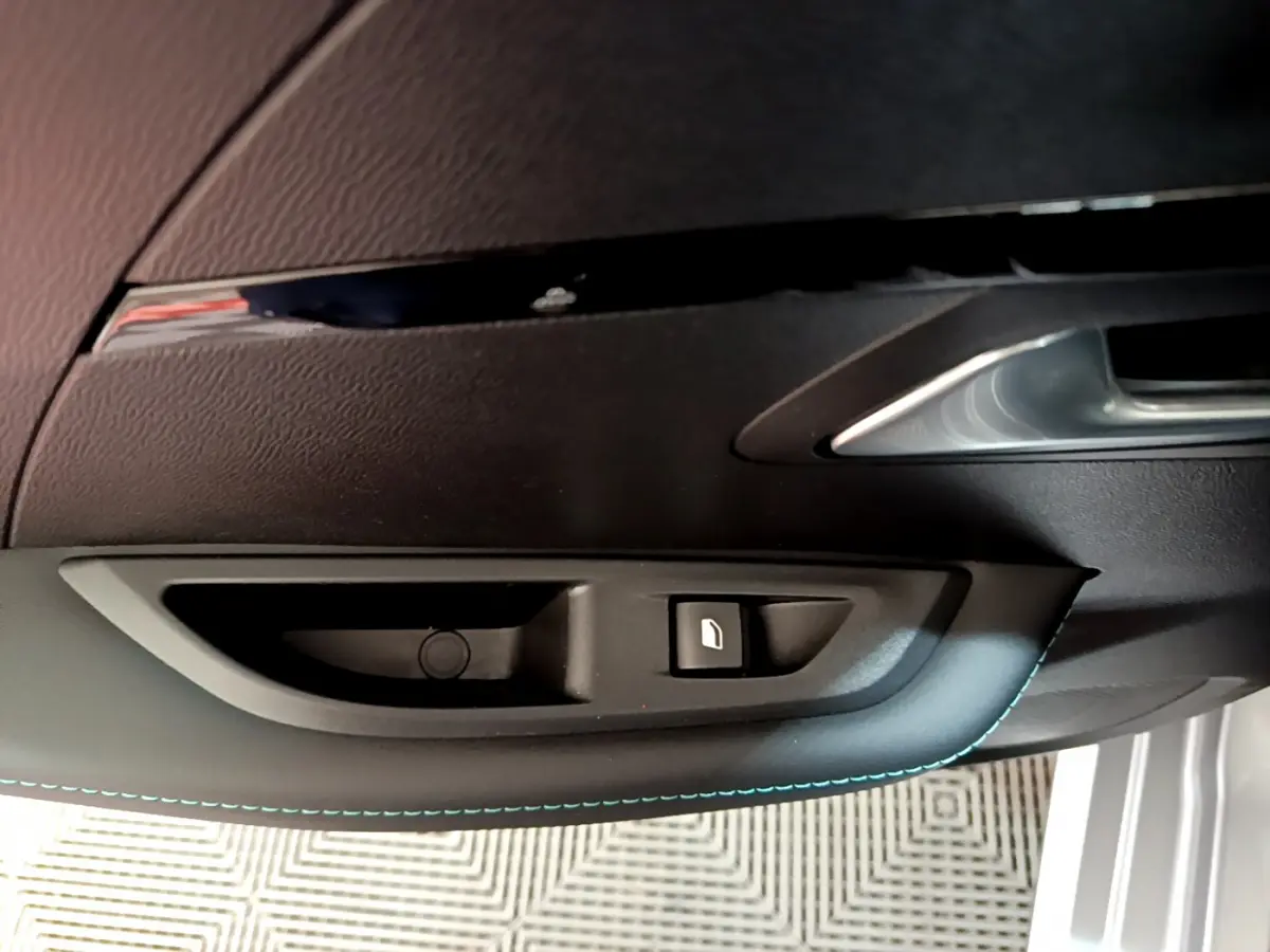 Détail de la commande de lève-vitre sur la portière avant droite d'une Peugeot 208 gris clair.