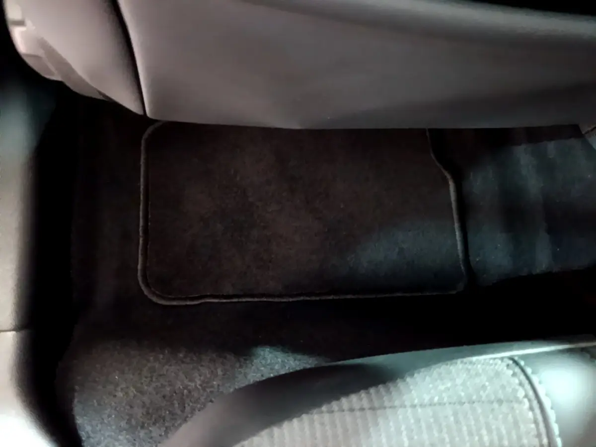 Gros plan sur le tapis de sol noir et le frein à main cuir dans l'habitacle d'une Peugeot 208 gris clair.