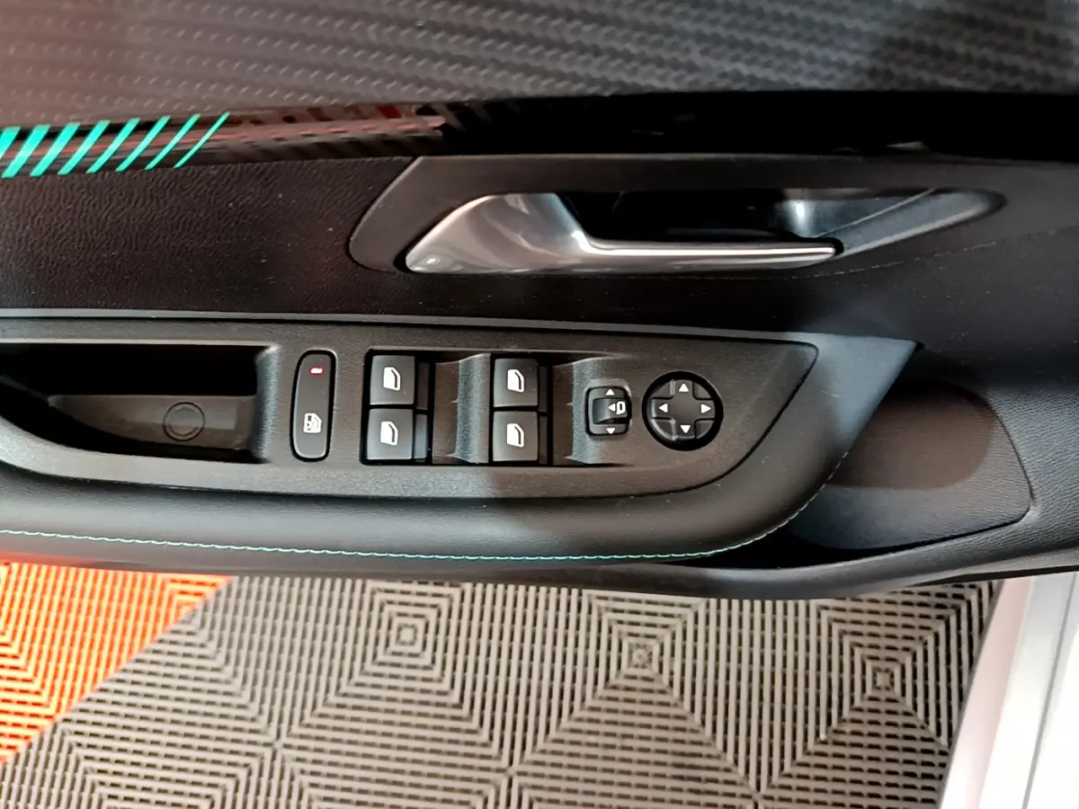 Vue rapprochée de la porte côté gauche d'une Peugeot 208 gris clair, montrant les commandes électriques des vitres et rétroviseurs.