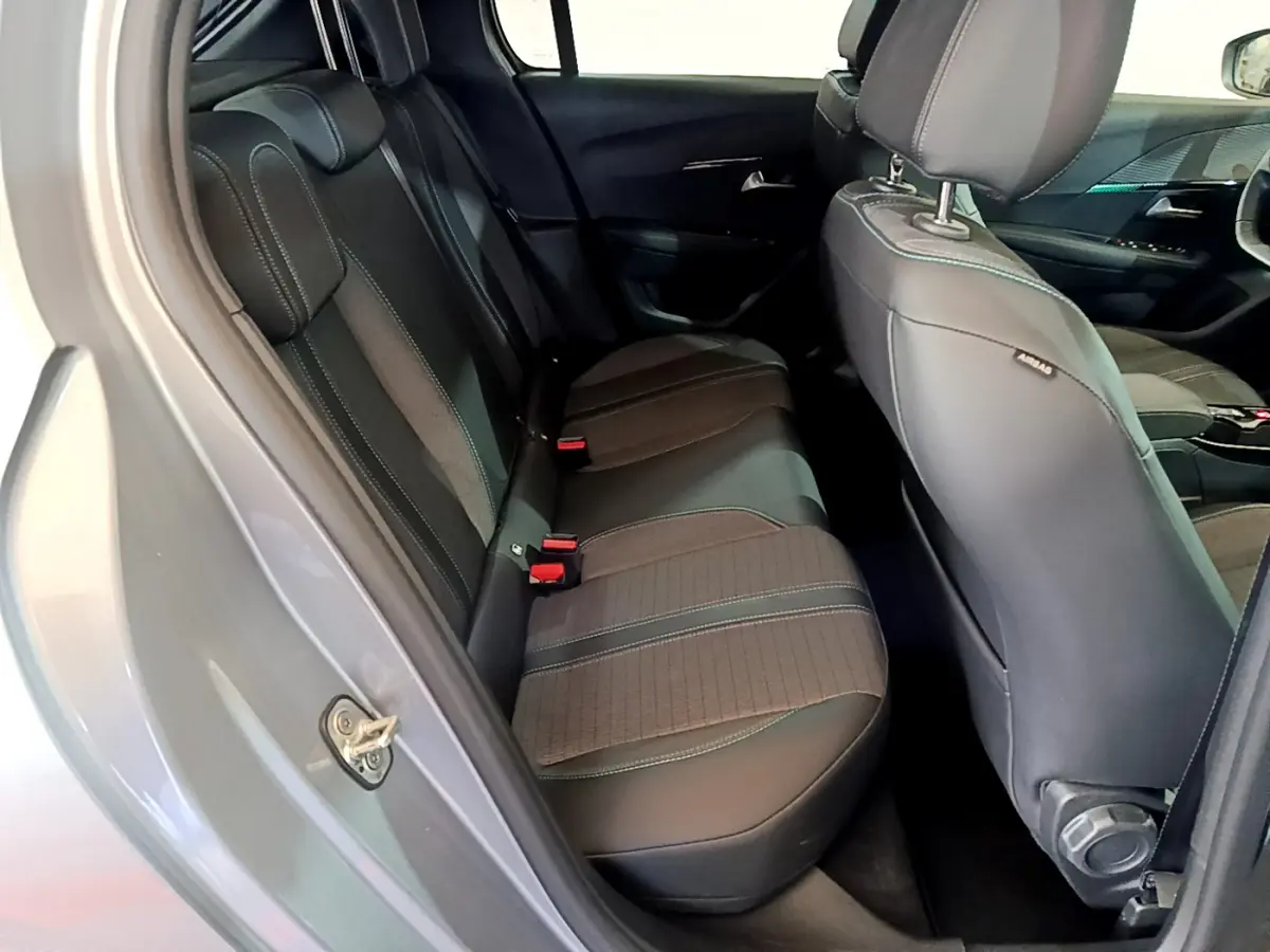 Vue intérieure côté arrière gauche de la Peugeot 208 gris clair, montrant la banquette arrière en tissu et cuir avec ceintures rouges.