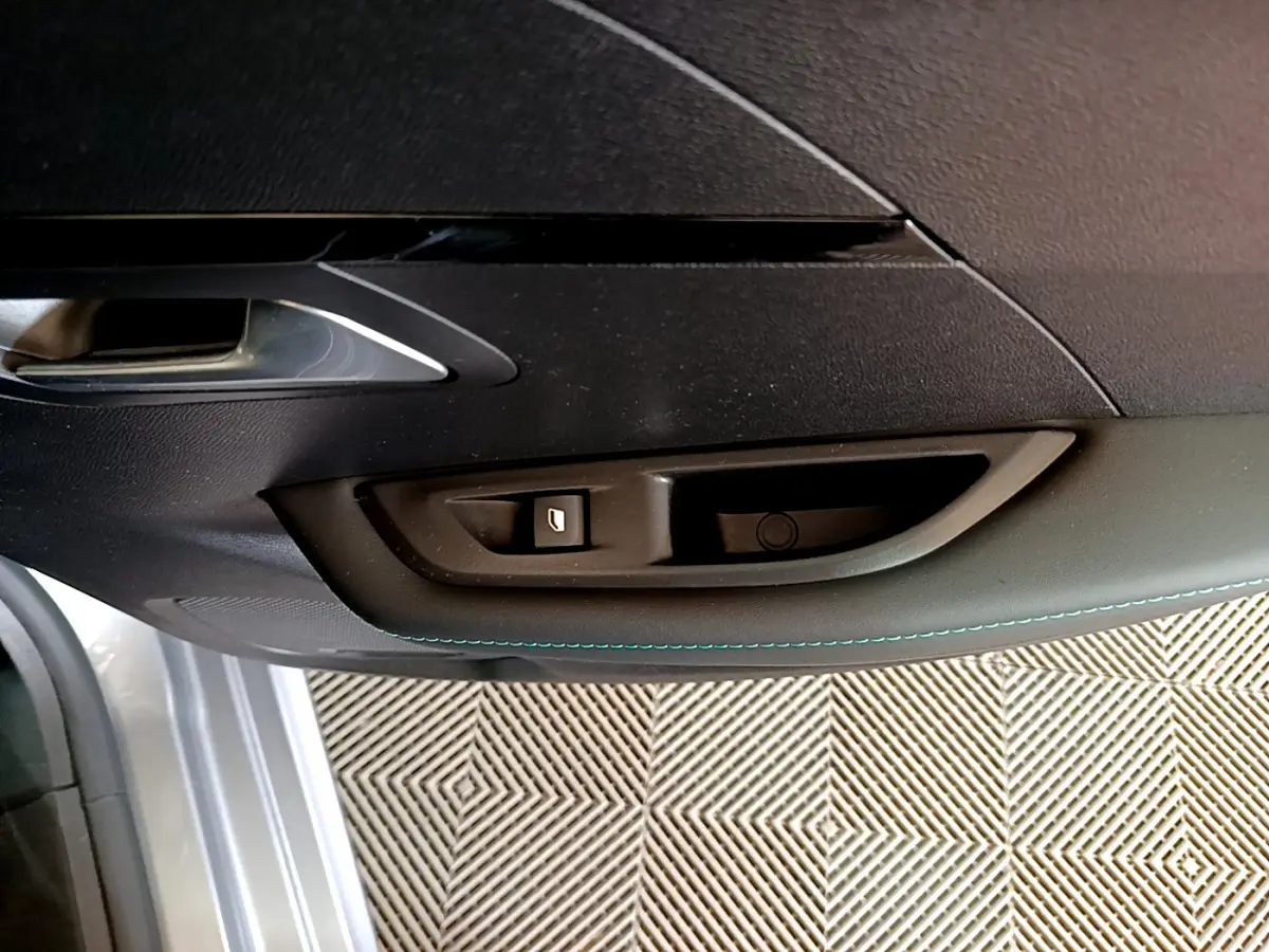 Gros plan sur la poignée intérieure et le bouton de lève-vitre côté conducteur d'une Peugeot 208 gris clair 2020.