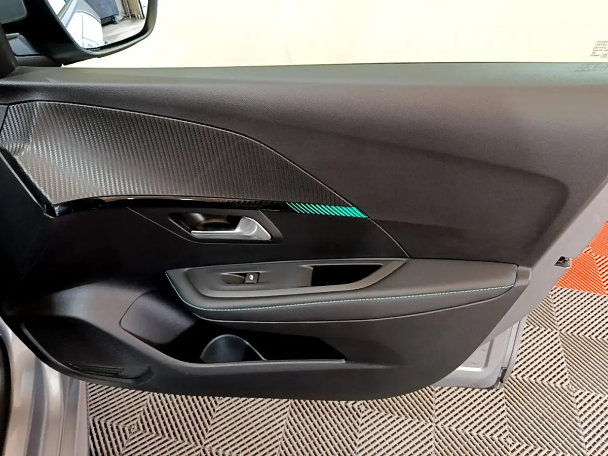 Gros plan sur la porte côté conducteur de la Peugeot 208 gris clair, avec insert carbone et surpiqûres bleues.