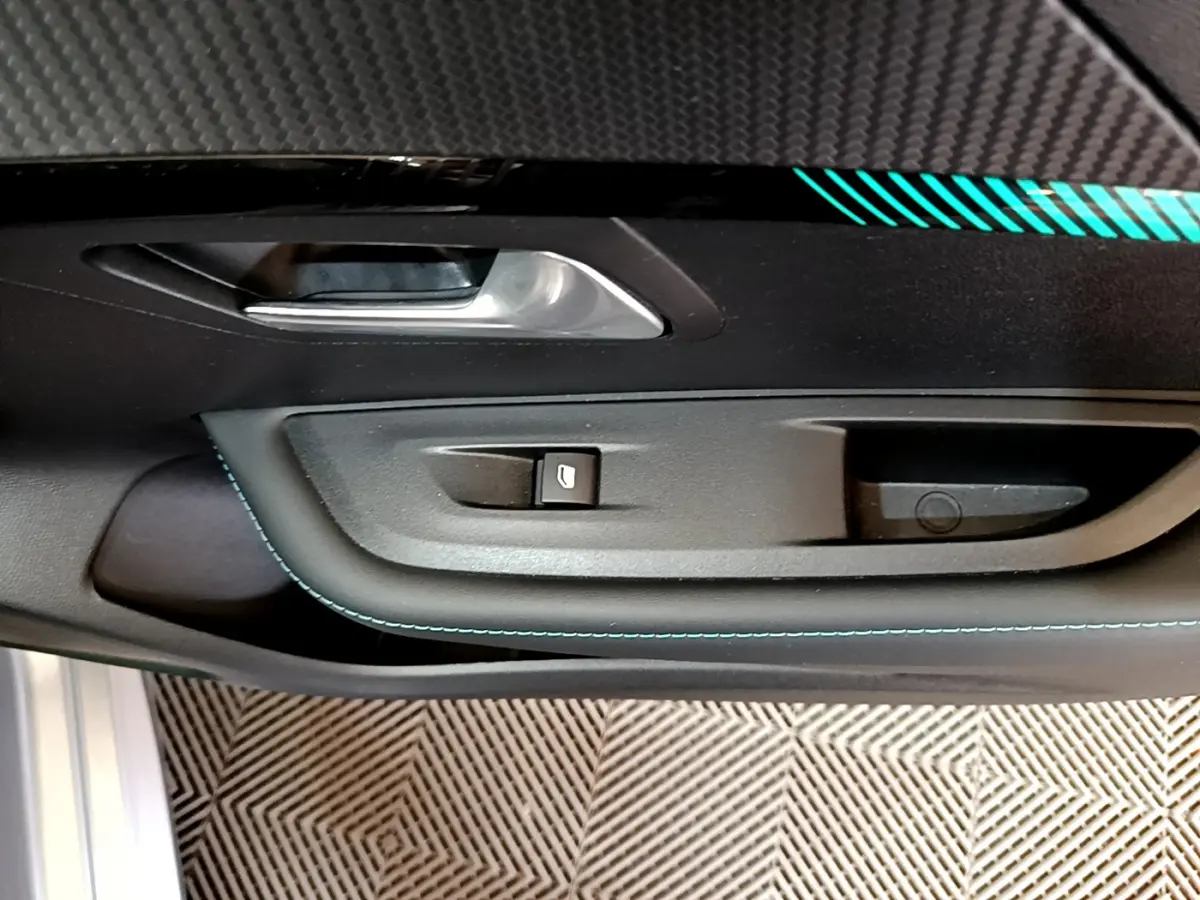 Gros plan sur la poignée intérieure côté conducteur de la Peugeot 208 gris clair avec surpiqûres bleues et bouton de vitre électrique.