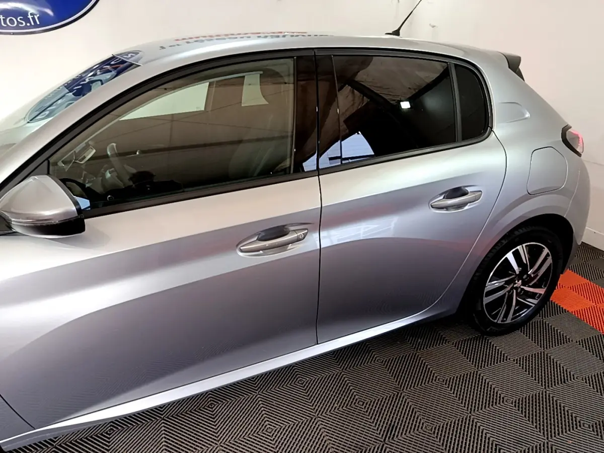 Profil côté gauche de la Peugeot 208 gris clair 2020, mettant en valeur les vitres teintées et les jantes alliage noires.