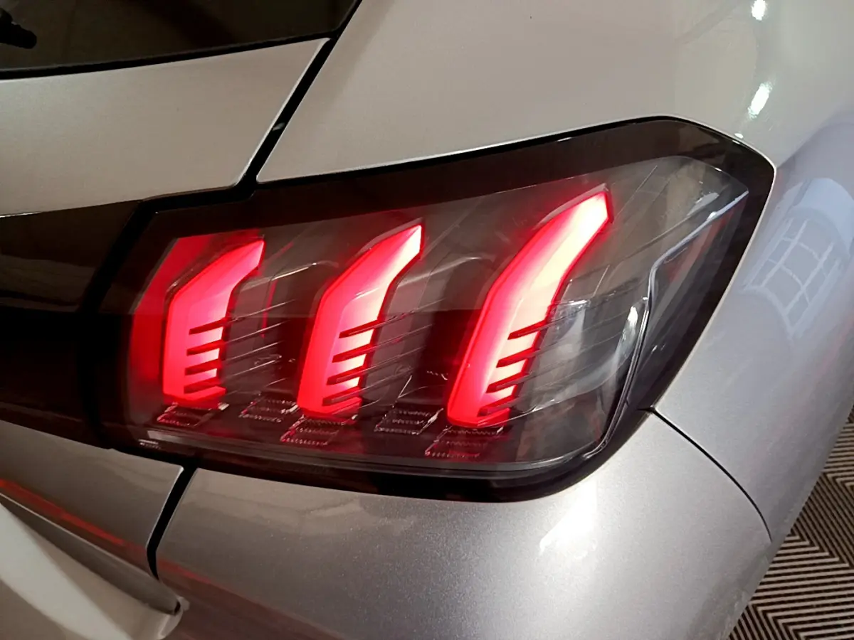 Gros plan sur le feu arrière droit rouge vif d'une Peugeot 208 gris clair, version PureTech 100 S&S Allure Business.