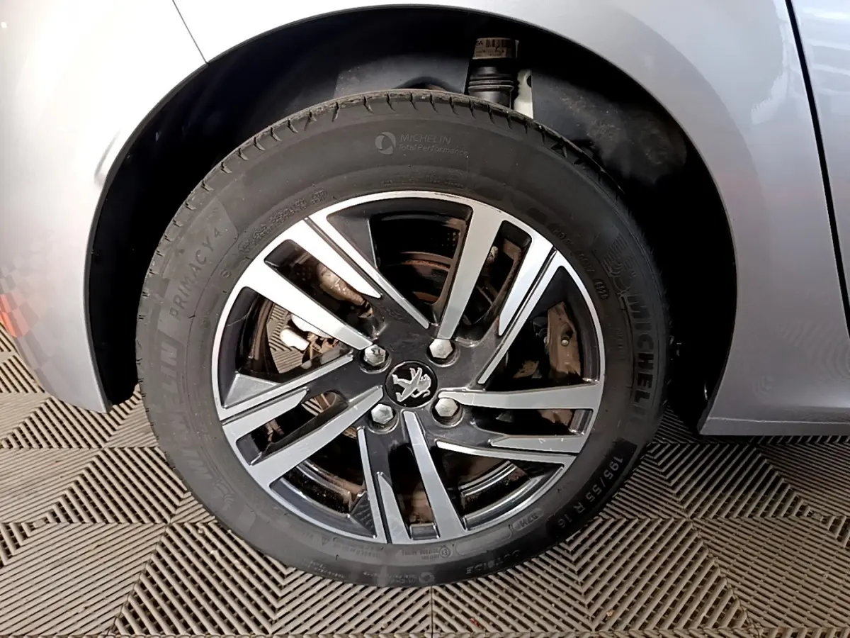 Gros plan sur la roue avant gauche gris clair d'une Peugeot 208 PureTech 100 S&S Allure Business avec jante alliage.