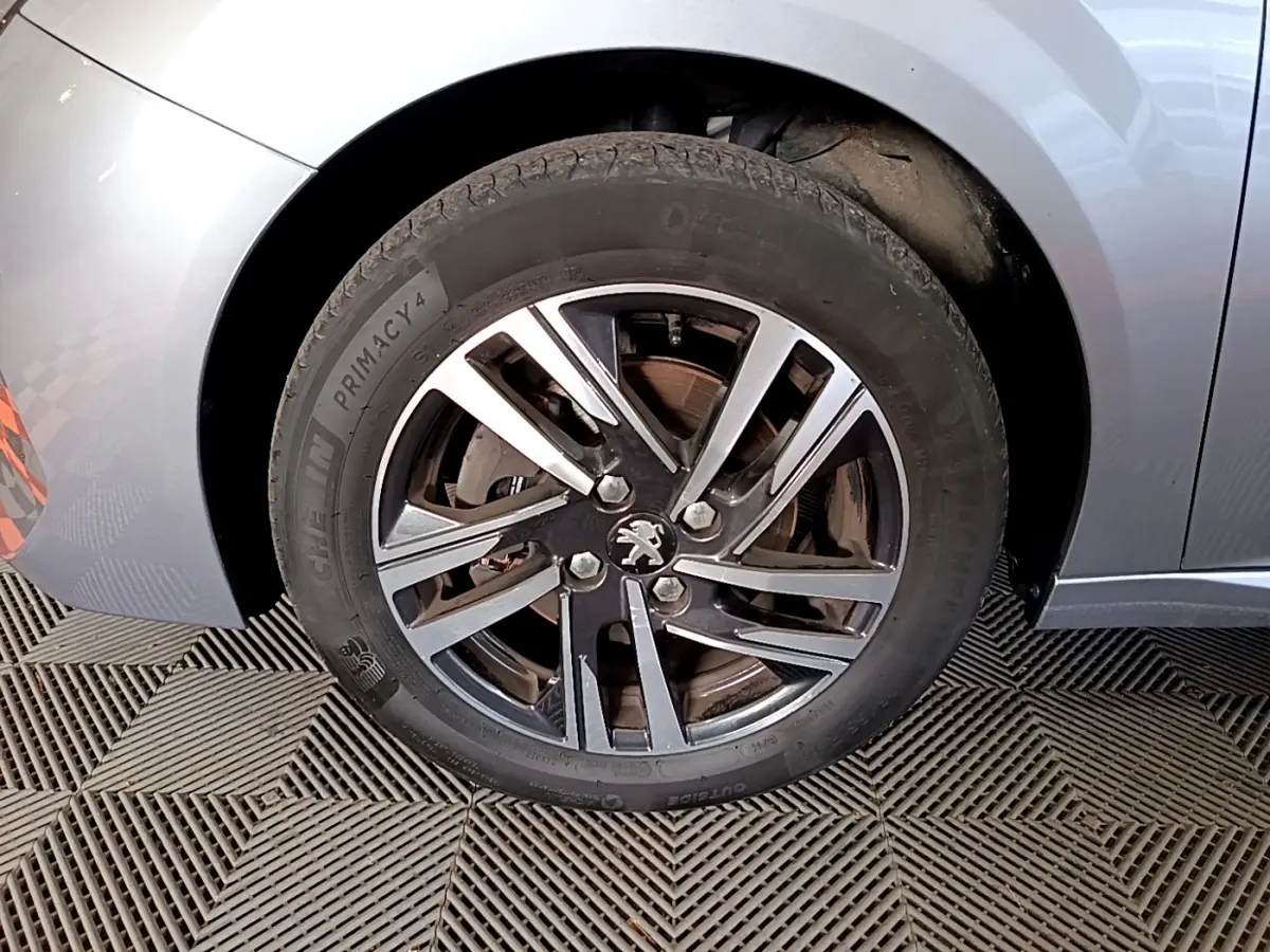 Gros plan sur la roue avant gauche gris clair de la Peugeot 208 avec jante alliage et logo lion au centre