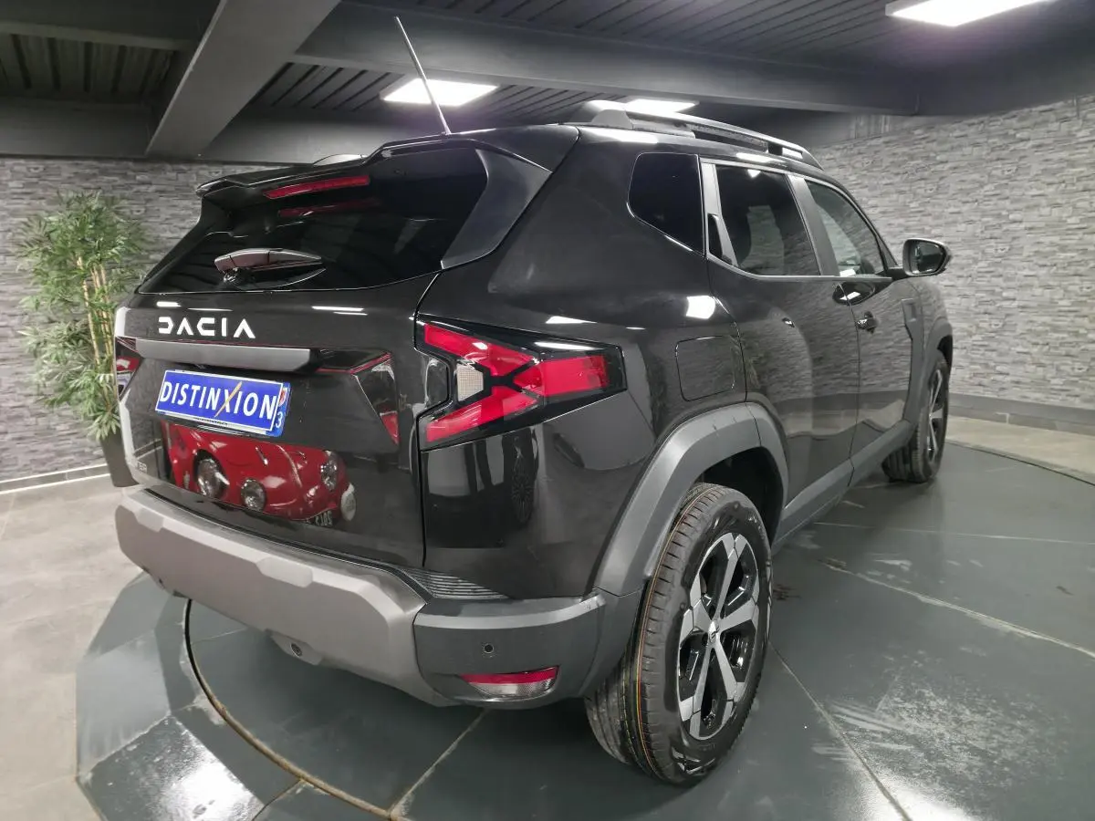 Vue 3/4 arrière droite d'un Dacia Duster 1.6 Hybrid noir nacré avec barres de toit noires et jantes alliage 18 pouces.