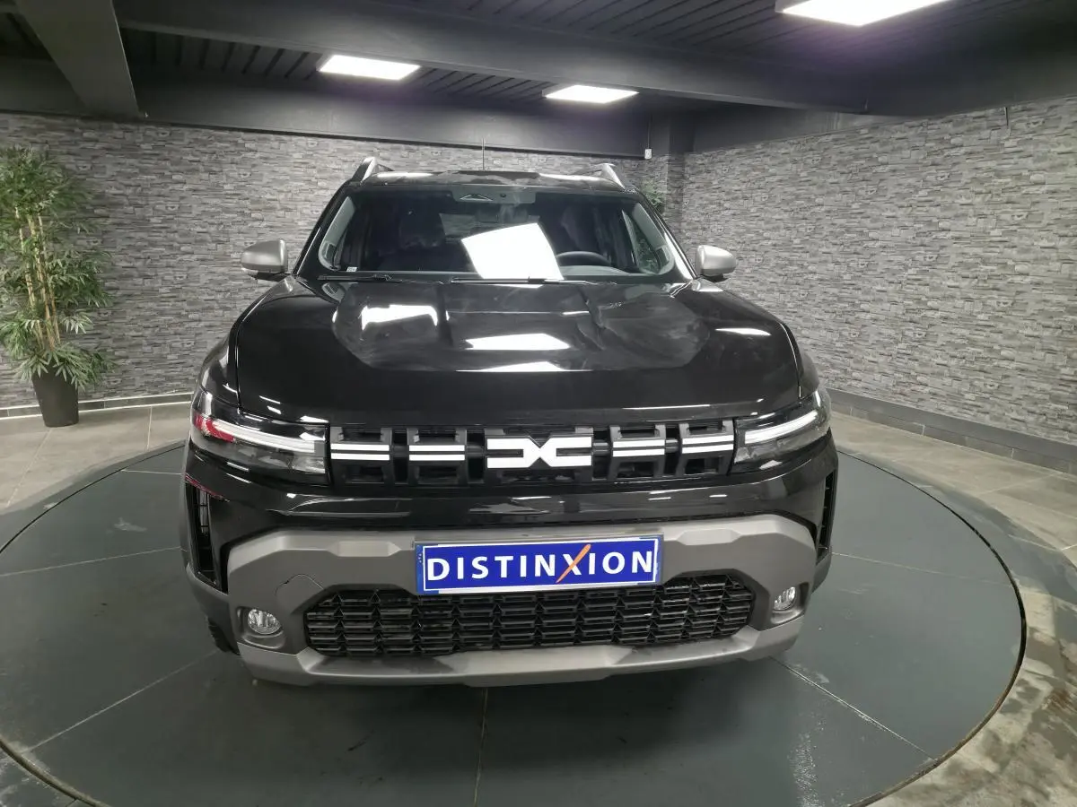 Vue avant d'un Dacia Duster 1.6 Hybrid noir nacré avec calandre noire et bouclier gris, en showroom intérieur.
