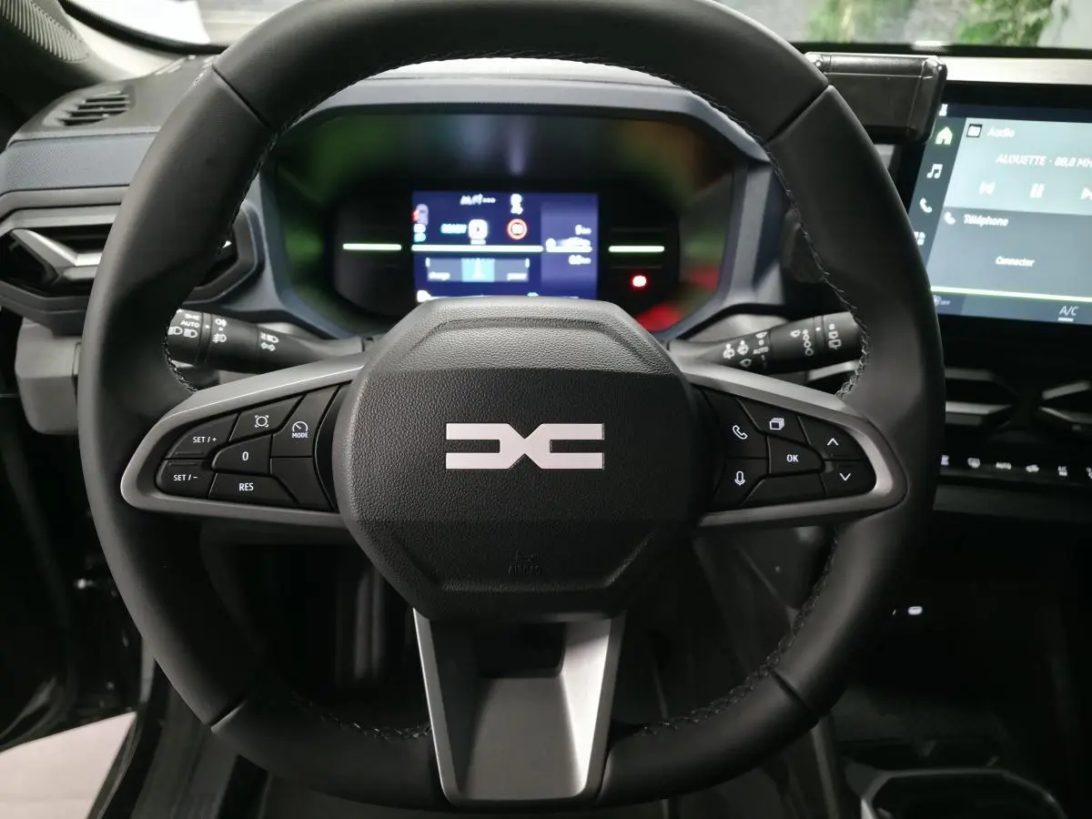 Vue rapprochée du volant noir du Dacia Duster 1.6 Hybrid 2025 avec commandes intégrées et tableau de bord digital.