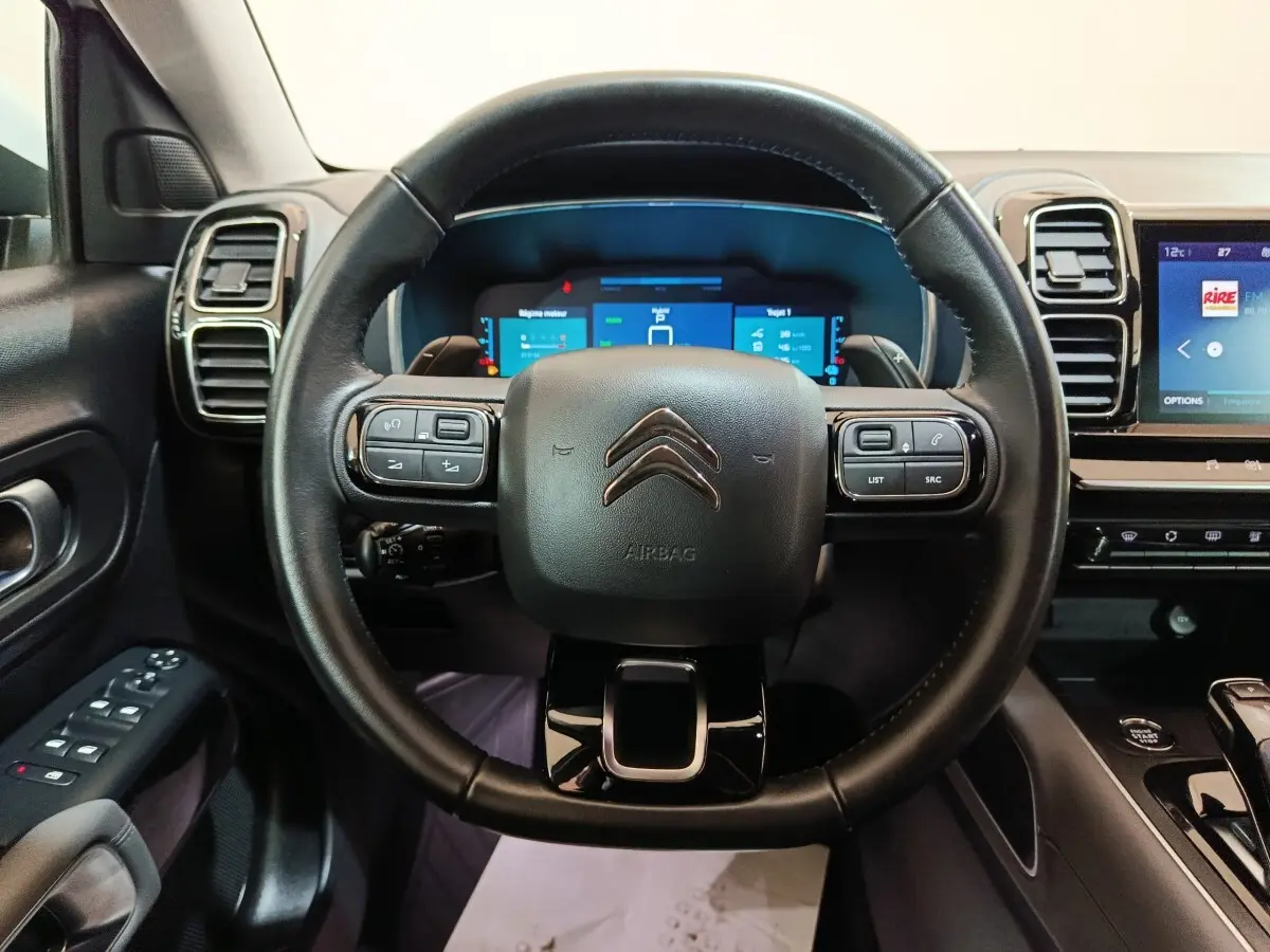 Vue intérieure centrée sur le volant noir du Citroën C5 Aircross Hybrid avec tableau de bord numérique et écran tactile.