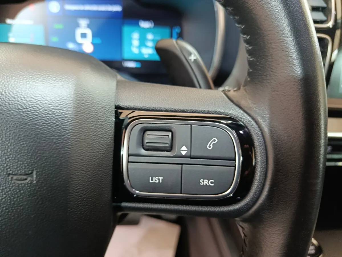Gros plan sur les commandes gauche du volant noir du Citroën C5 Aircross Hybrid 225 ë-EAT8 avec affichage numérique en arrière-plan.