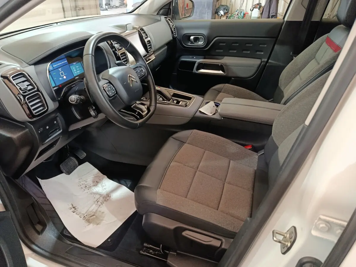 Intérieur côté conducteur du Citroën C5 Aircross Hybrid blanc, avec tableau de bord numérique et sièges gris tissu.