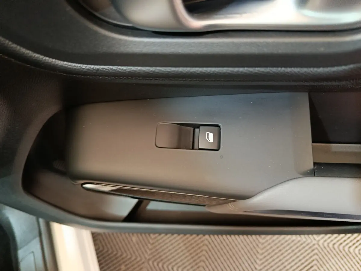 Gros plan sur le bouton de commande de vitre électrique côté conducteur dans l'intérieur noir du Citroën C5 Aircross blanc hybride.