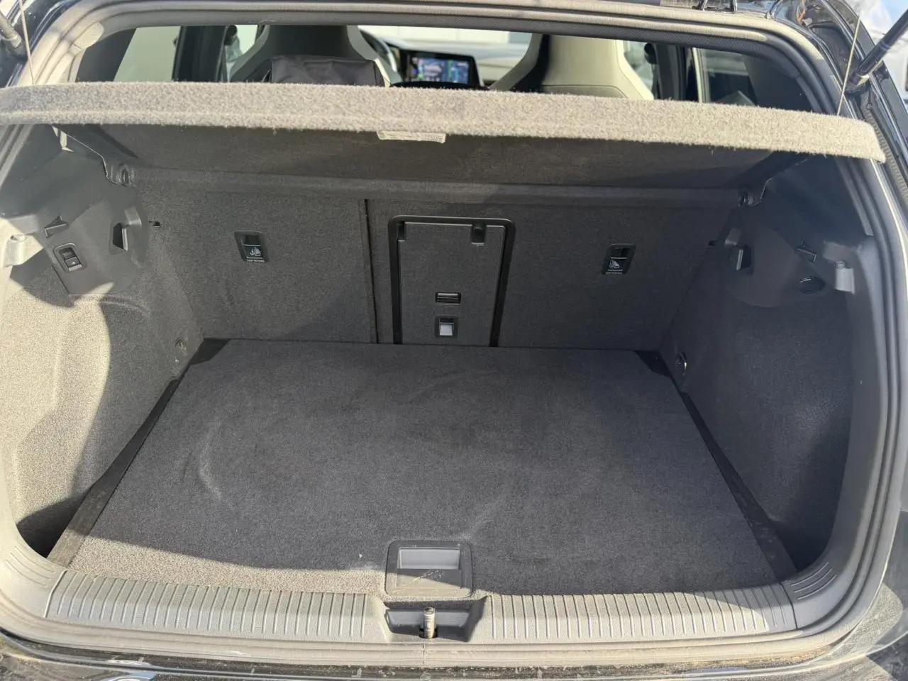 Coffre ouvert vu de l'arrière d'une Volkswagen Golf 8 noire, montrant l'espace de chargement et la tablette arrière.