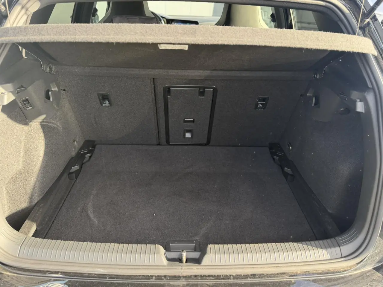 Coffre ouvert vu de l'arrière d'une Volkswagen Golf 8 noire, montrant un espace de chargement vide et propre.
