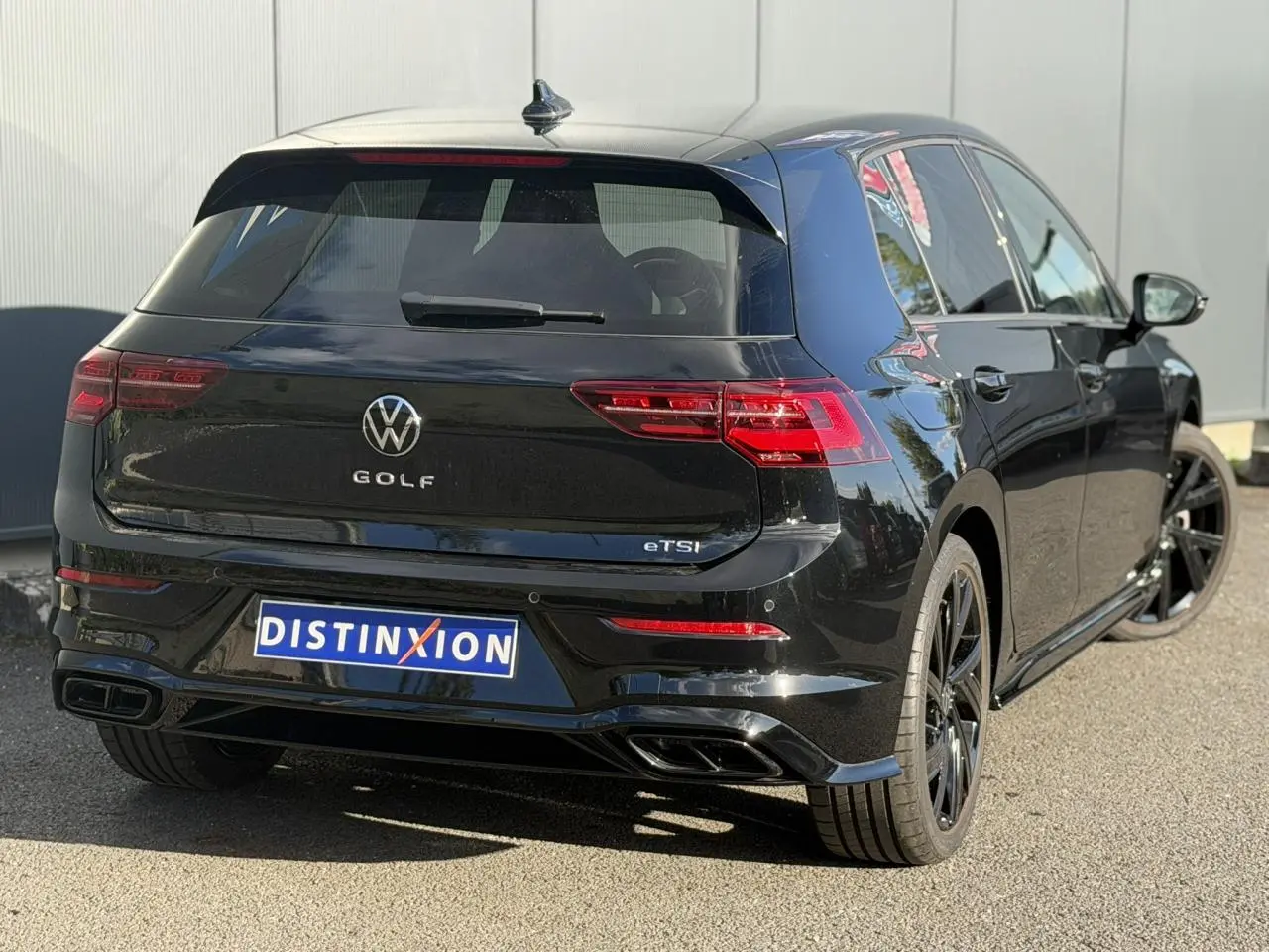 Vue 3/4 arrière droite d'une Volkswagen Golf 8 noire avec jantes noires et double sortie d'échappement R-Line.
