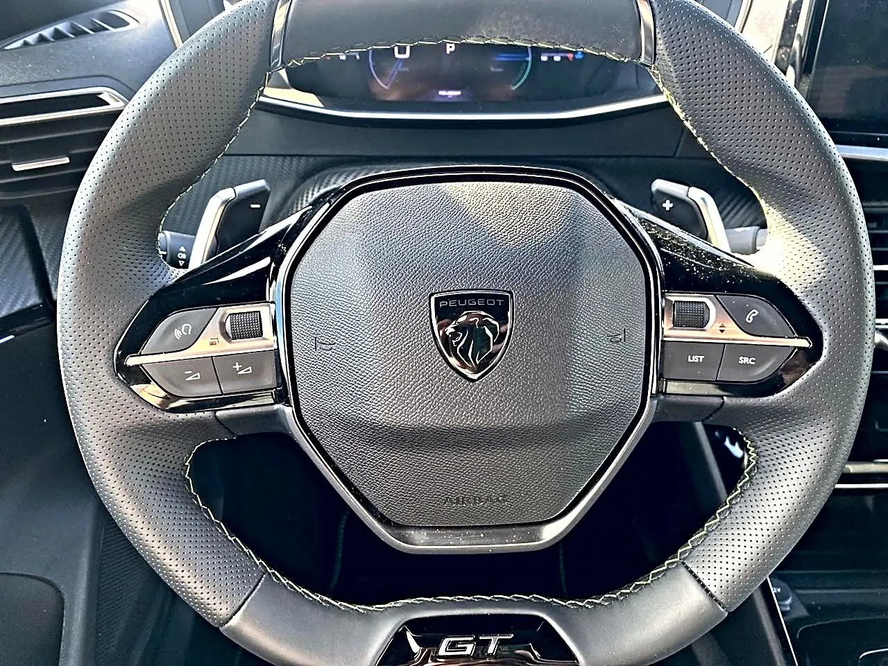 Vue rapprochée du volant cuir noir perforé du Peugeot 2008 1.2 hybrid 145 GT avec logo et commandes intégrées.