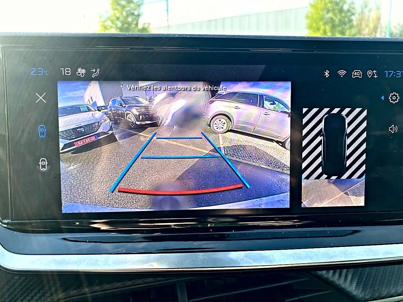 Écran tactile montrant la caméra de recul d’un Peugeot 2008 noir avec guidage de trajectoire en bleu et rouge.