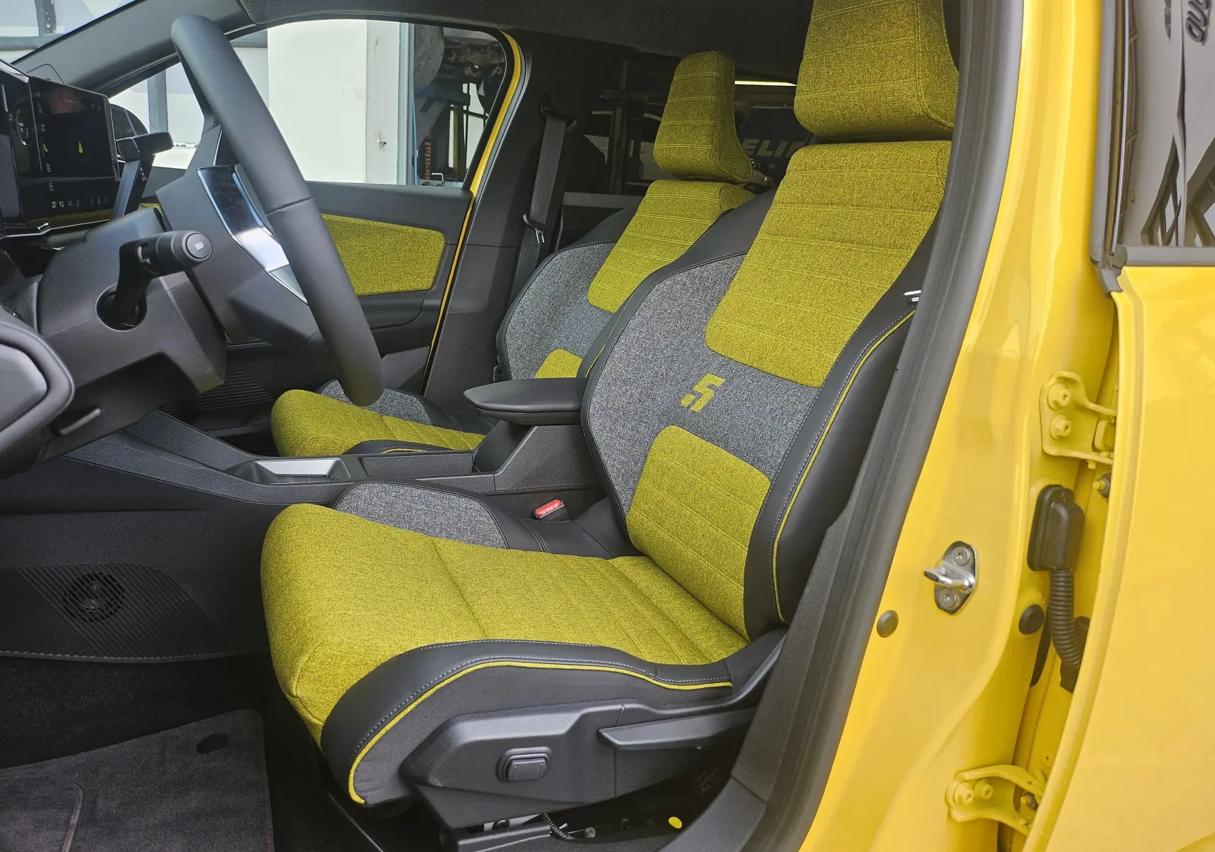Vue intérieure côté conducteur de la Renault R5 Iconic 2025, sièges tissu jaune pop et gris avec logo "5" brodé.