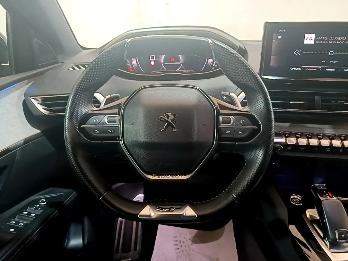 Vue rapprochée du volant cuir noir GT et tableau de bord numérique du Peugeot 5008 bleu 2021.