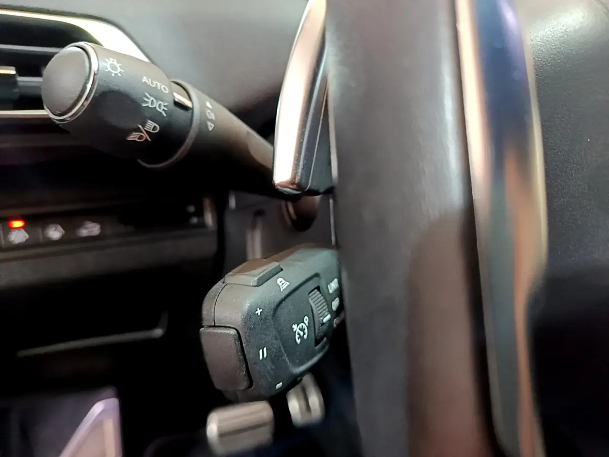 Gros plan sur la commande multifonction du volant cuir à gauche dans l'habitacle du Peugeot 5008 bleu 2021.