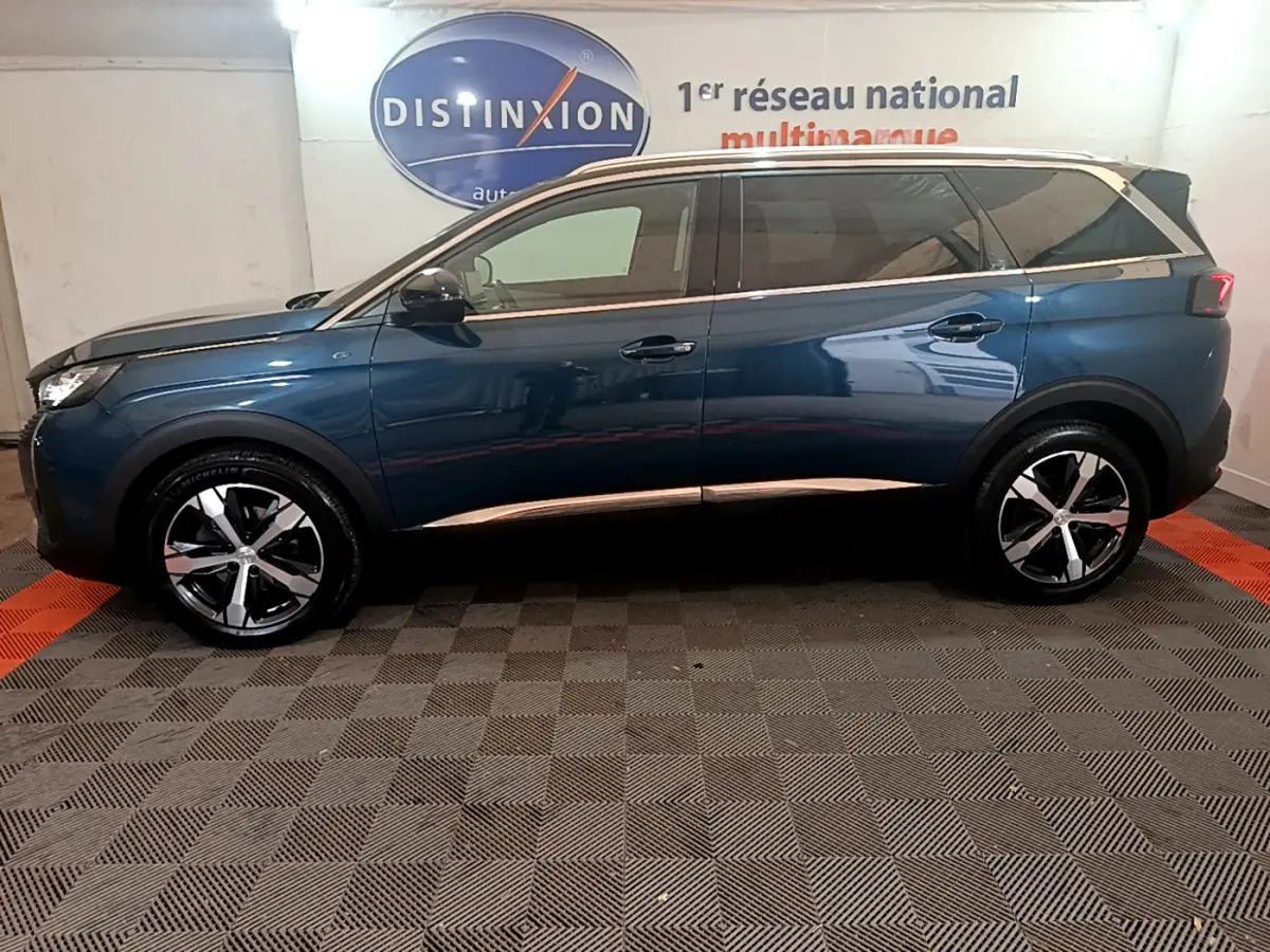 Profil côté gauche d'un Peugeot 5008 bleu 2021 avec jantes alliage et vitres teintées en intérieur showroom