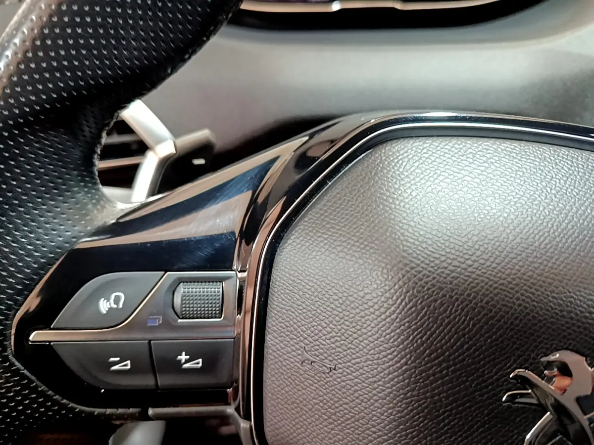 Gros plan sur le volant cuir noir perforé du Peugeot 5008 GT 2021 avec commandes audio intégrées côté gauche.