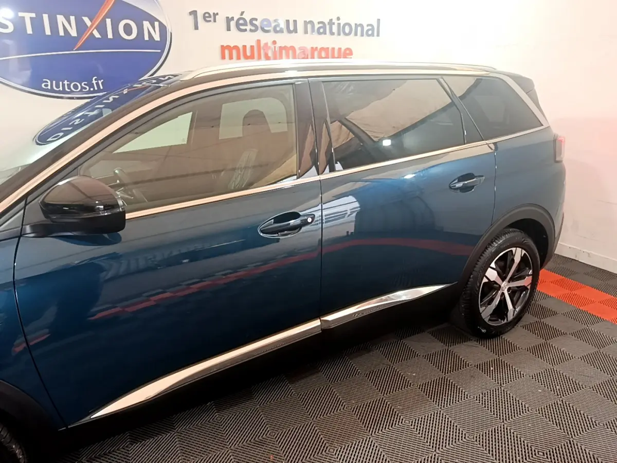 Profil côté gauche d'un Peugeot 5008 bleu 2021 avec jantes alliage et vitres teintées en intérieur showroom.