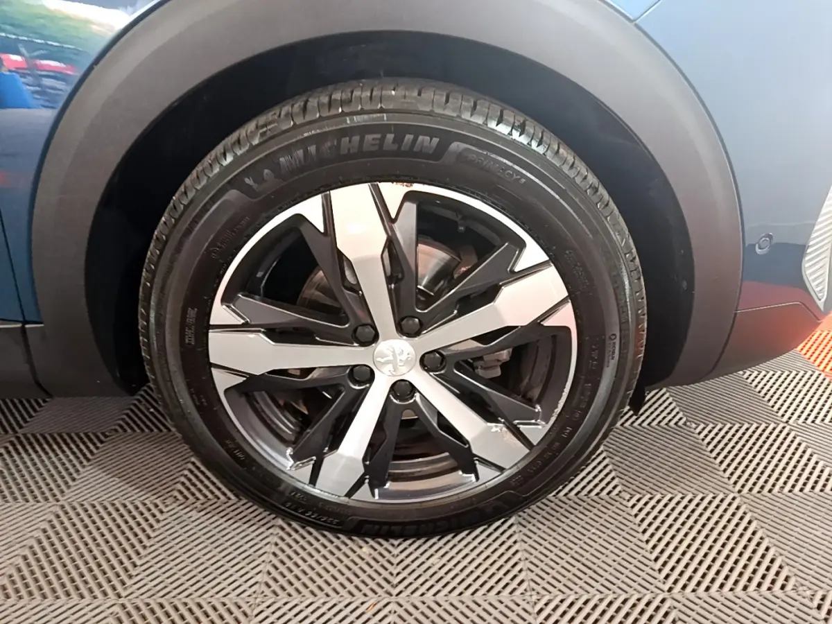 Gros plan sur la roue avant gauche du Peugeot 5008 bleu, avec jante alliage bicolore et pneu Michelin.