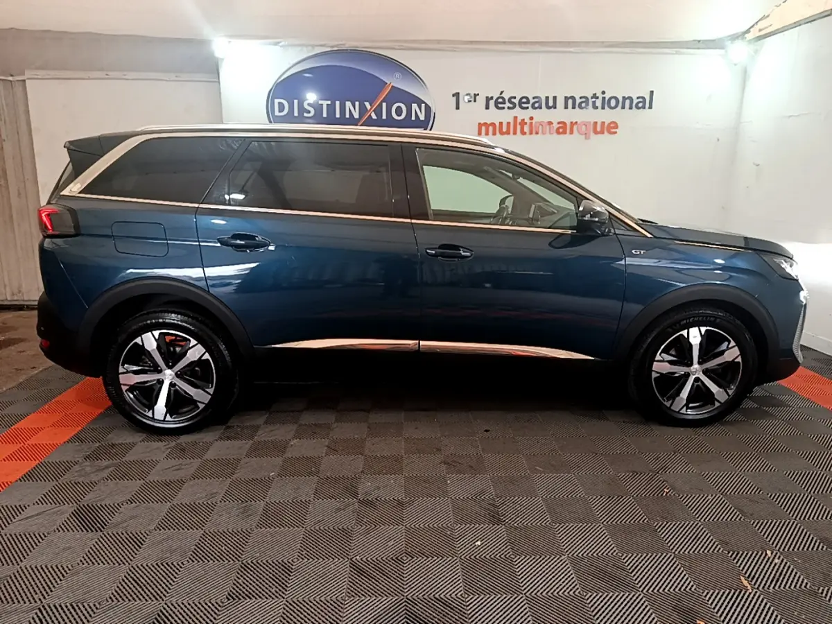 Profil côté droit d'un Peugeot 5008 GT bleu 2021 avec jantes alliage et toit noir en intérieur showroom