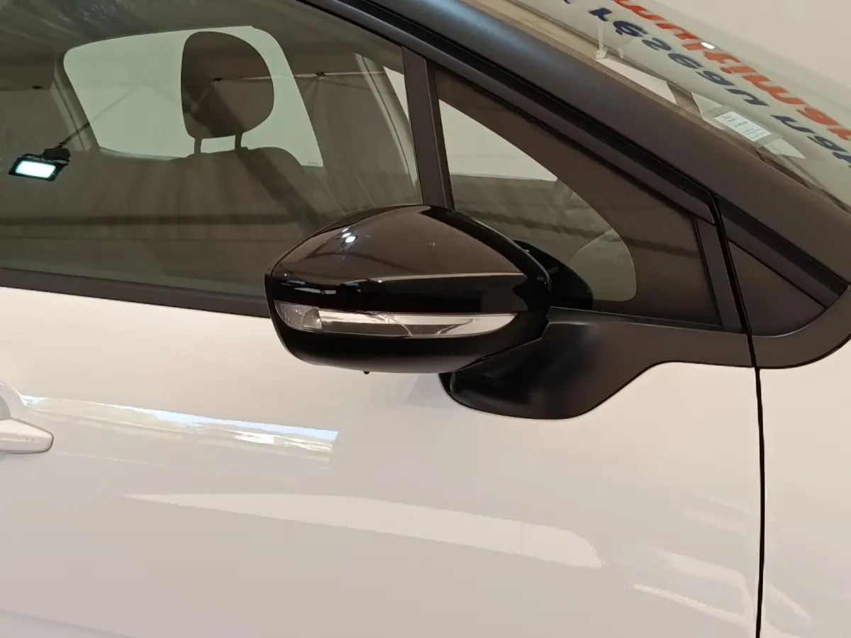 Gros plan sur le rétroviseur noir côté conducteur d'une Citroën C3 blanche, avec vitre teintée en arrière-plan.
