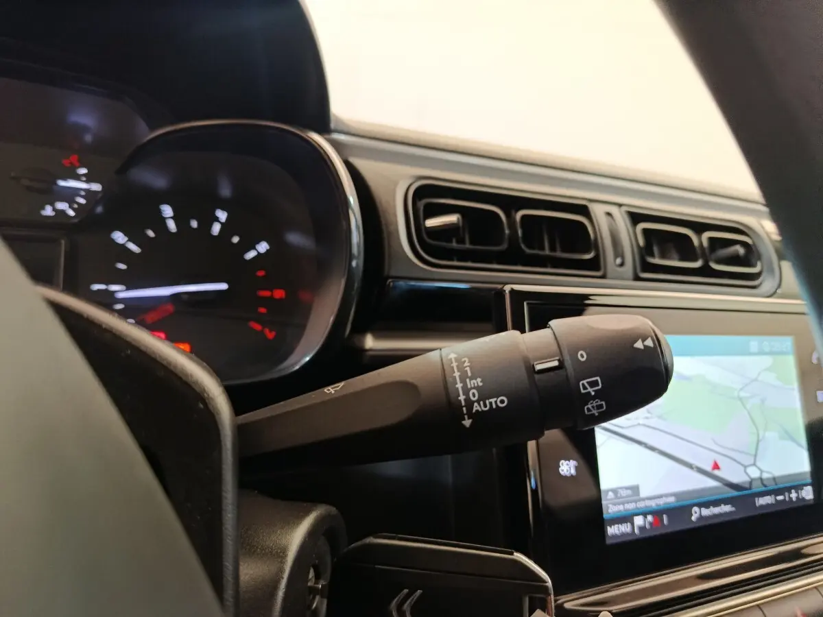 Détail du commodo d’essuie-glace dans l’habitacle d’une Citroën C3 blanche, avec tableau de bord et écran tactile de navigation.