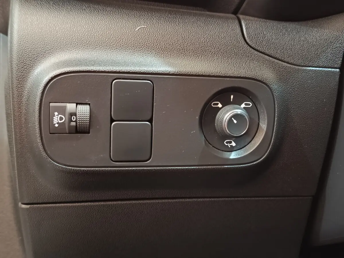 Gros plan sur les commandes de réglage des rétroviseurs et des phares dans l'habitacle noir d'une Citroën C3 blanche.