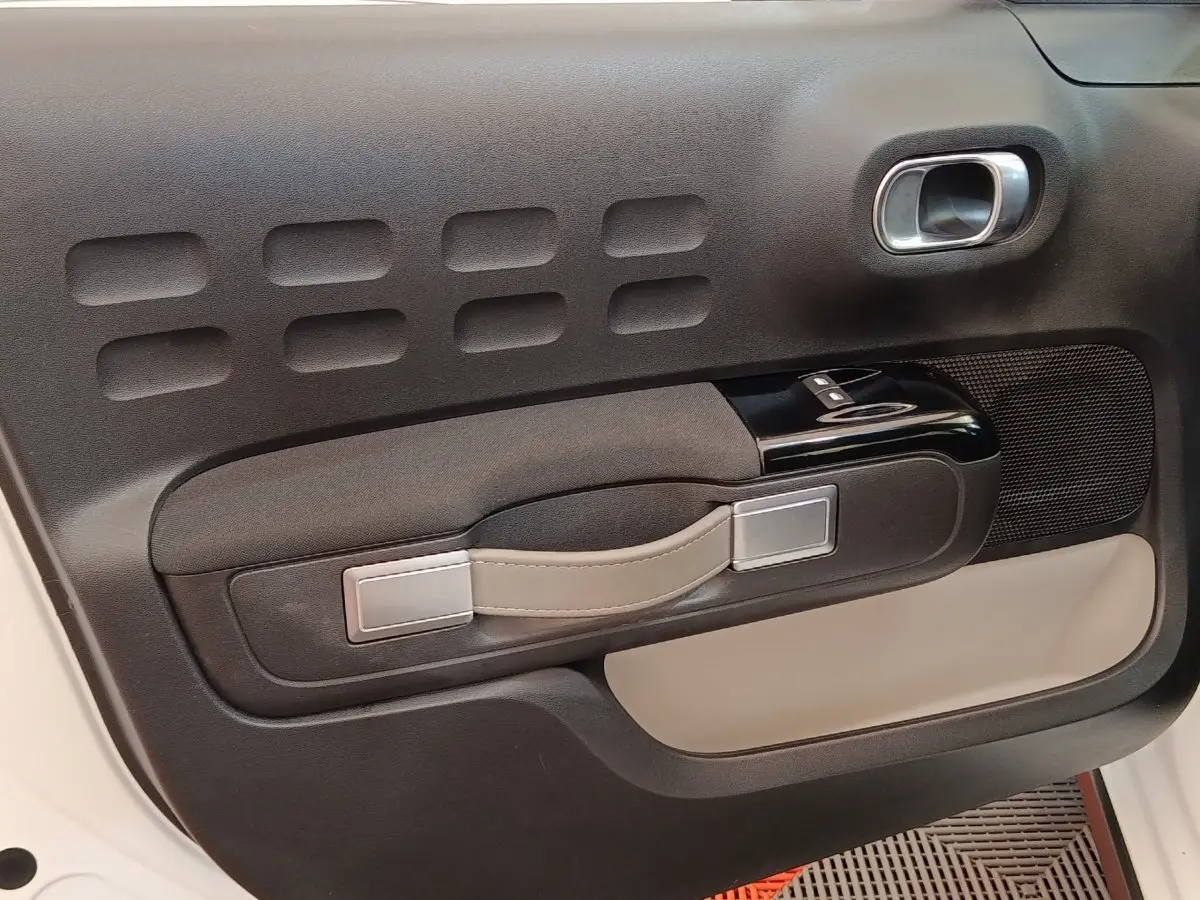 Gros plan sur la porte intérieure côté conducteur de la Citroën C3 blanche, avec poignée beige et commandes vitres noires.