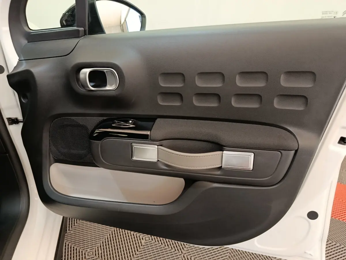 Vue intérieure côté gauche de la porte avant blanche de la Citroën C3 2020 avec poignée cuir et inserts noirs.